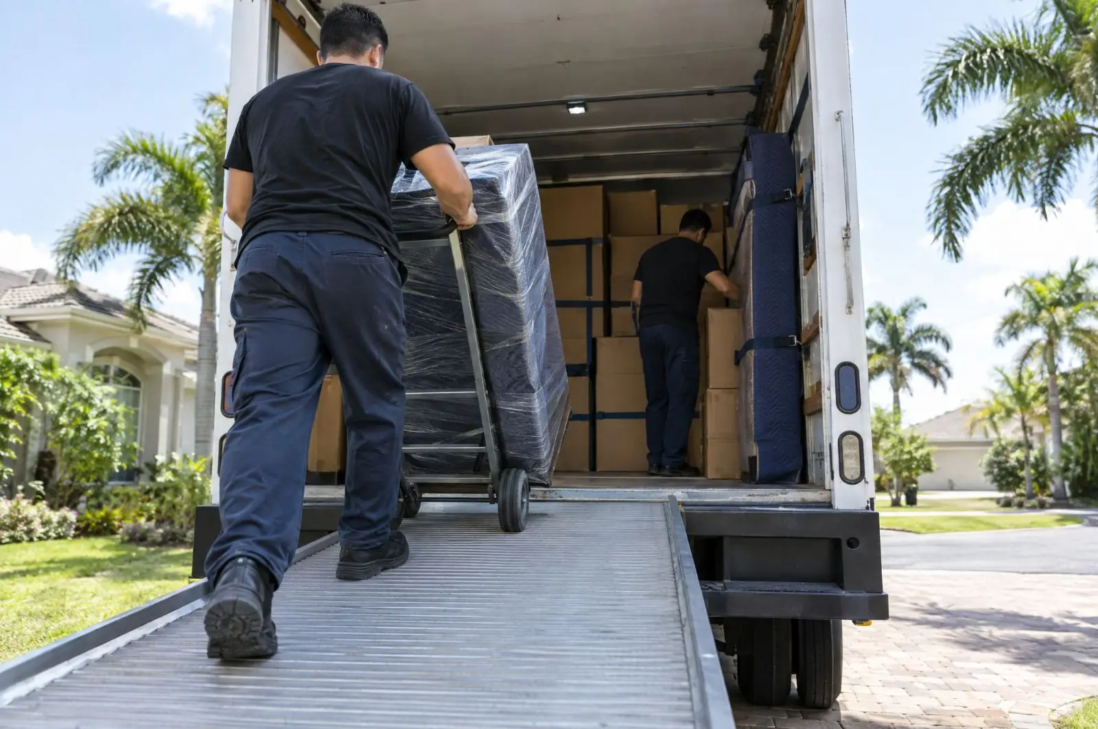 Mover rolling padded furniture up the ramp of a moving truck to load it